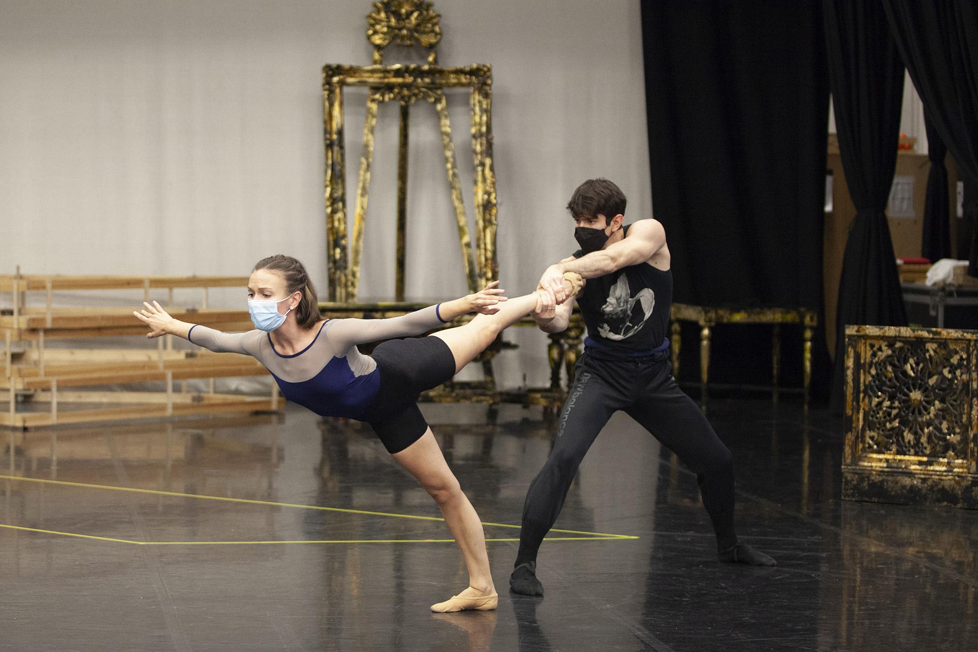 Dancer stands on one legt lean forward while being held steady by male dancer holding her raised foot