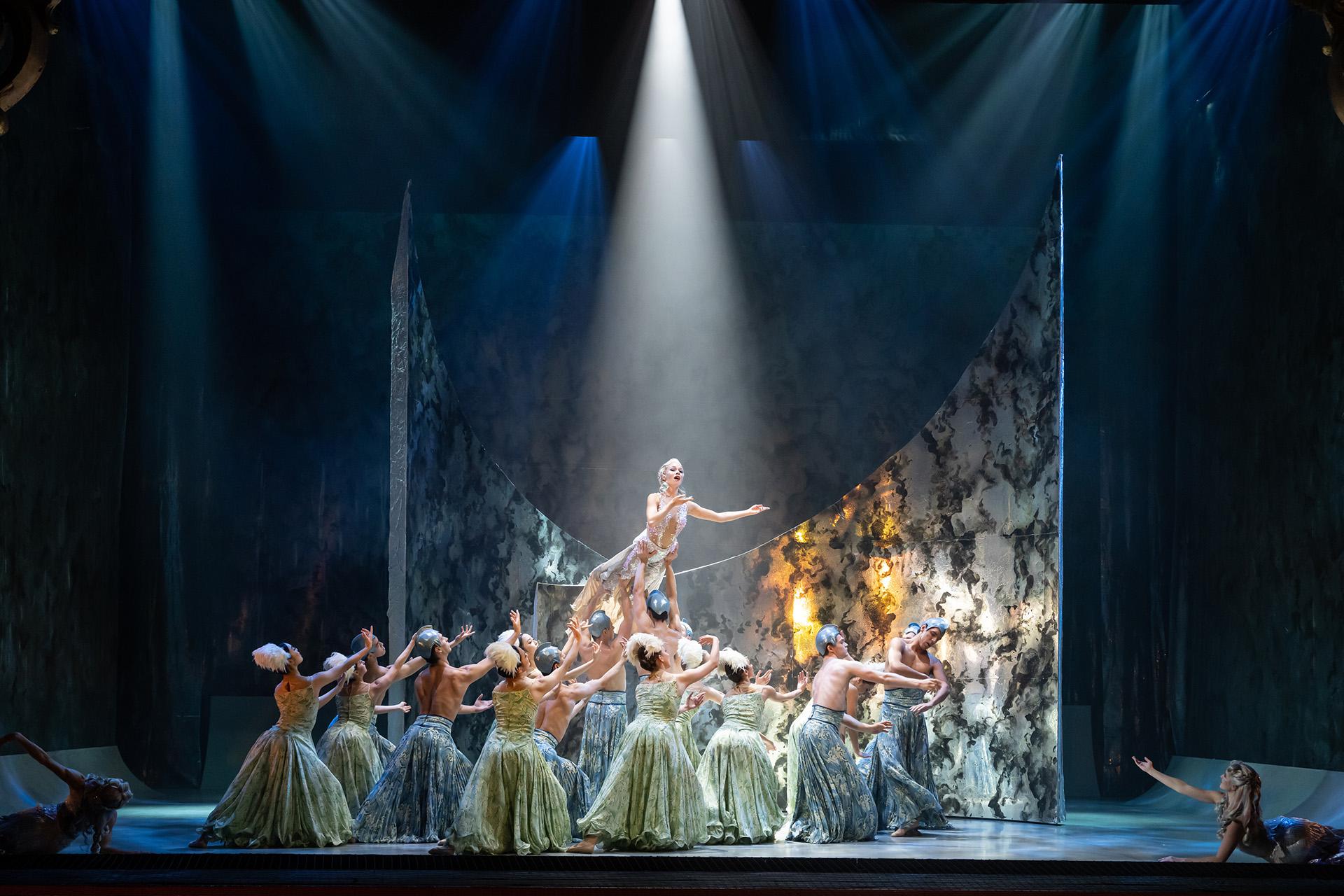 Dancers in skirts of blue and green representing the sea, support MArilla, light shining on her from above and singing